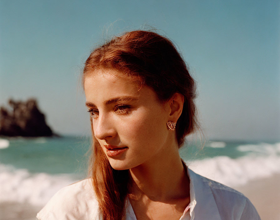 Brown-haired woman with earring at beach, white shirt, calm expression