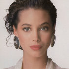 Portrait of woman with bob hairstyle, makeup, and gold earrings on cream background