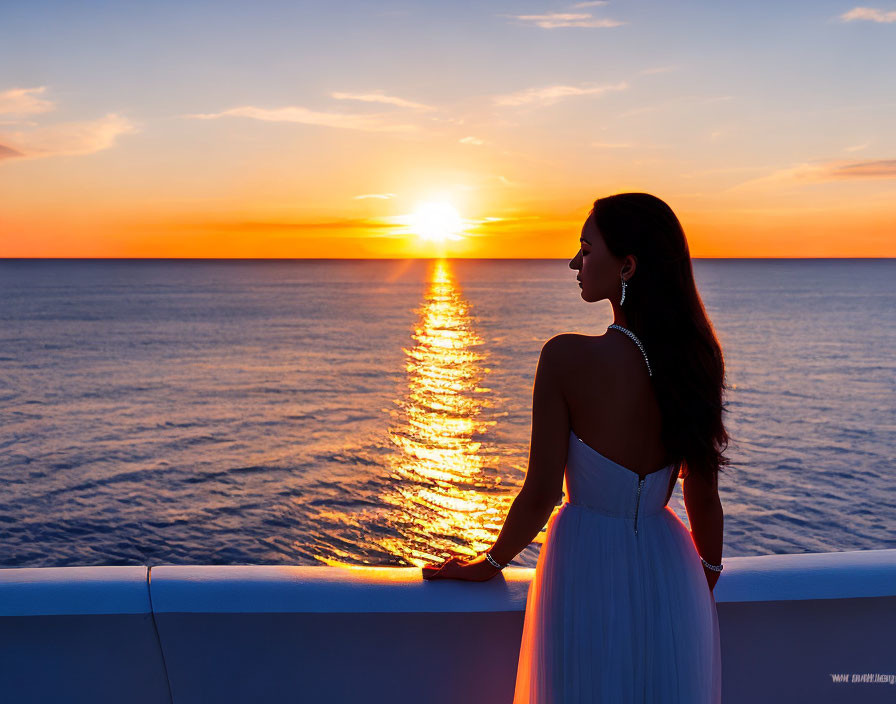 Woman in white dress gazes at ocean sunset from balcony