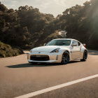 White sports car parked on mountain road with trees and sunlight.