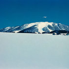 Snowy landscape with mountain backdrop and red-roofed houses under clear blue sky