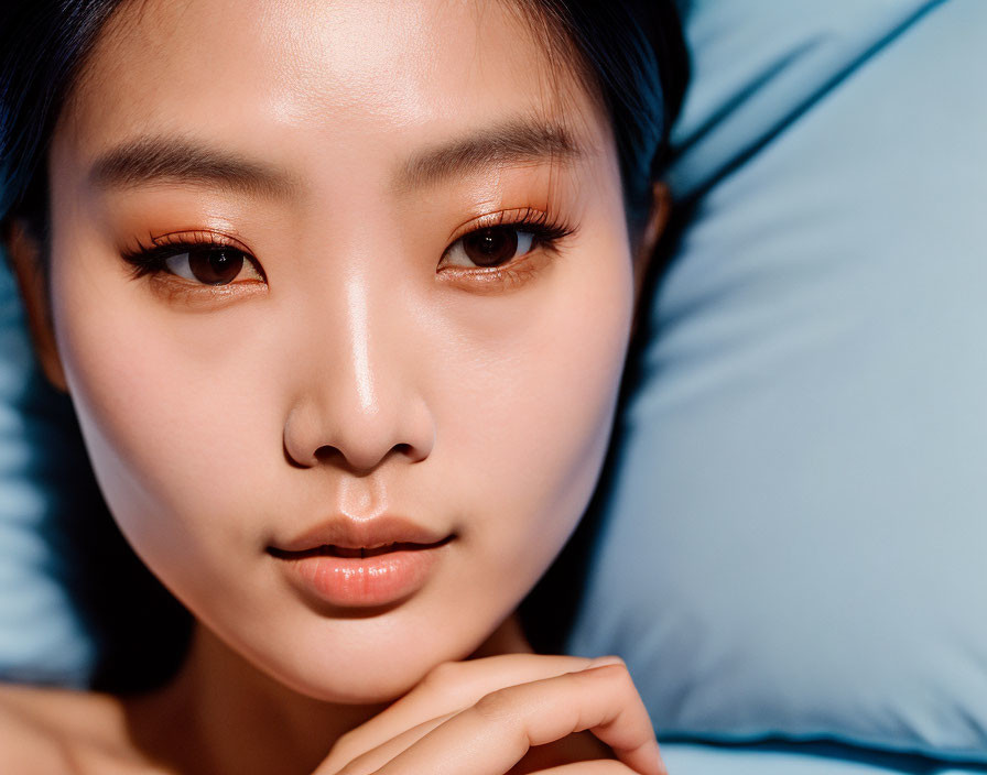 Asian woman with makeup on blue pillow gazes at camera