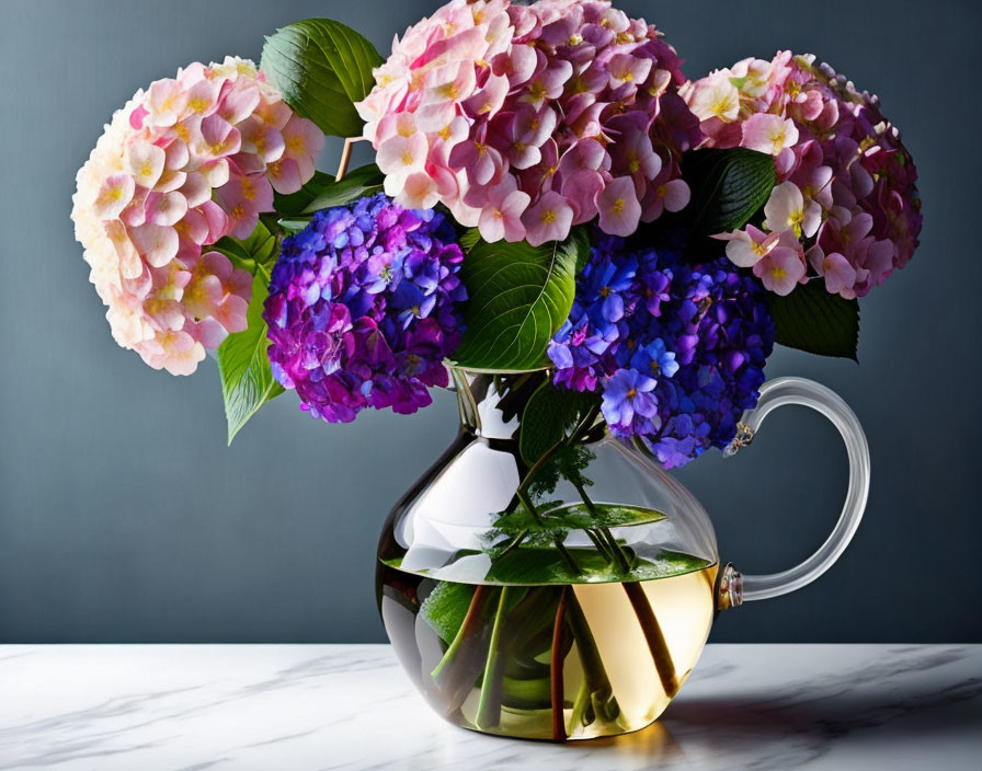 Pink and Blue Hydrangea Bouquet in Transparent Teapot on Marble Surface