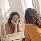 Young girl in yellow jacket gazes at reflection in ornate golden mirror