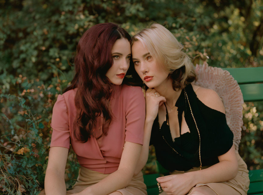 Two women on green bench in garden: one with dark red hair, pink top; other blonde in