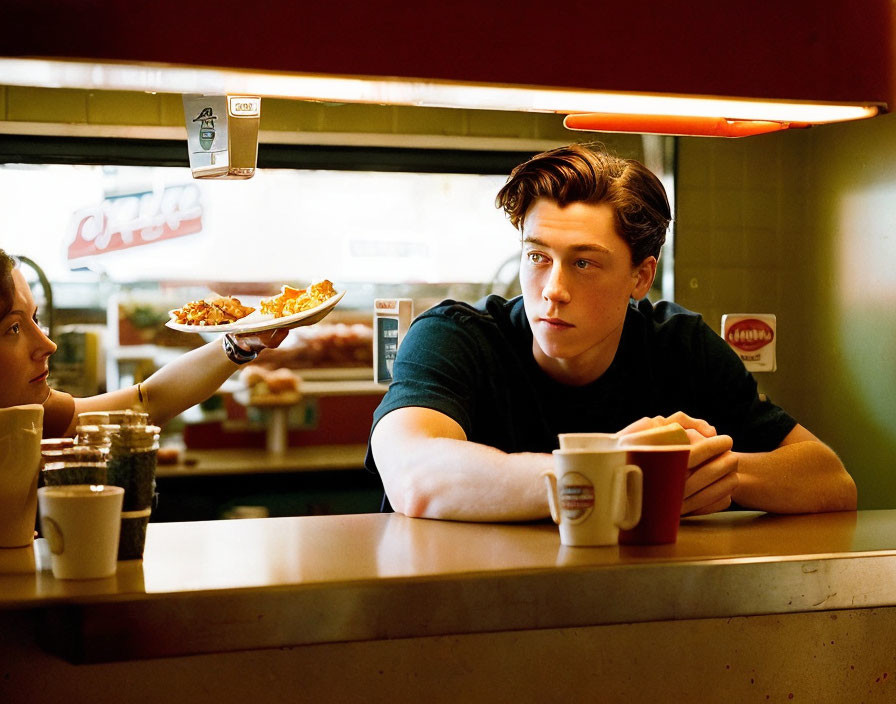 Young man with contemplative expression at diner counter offered pizza slice