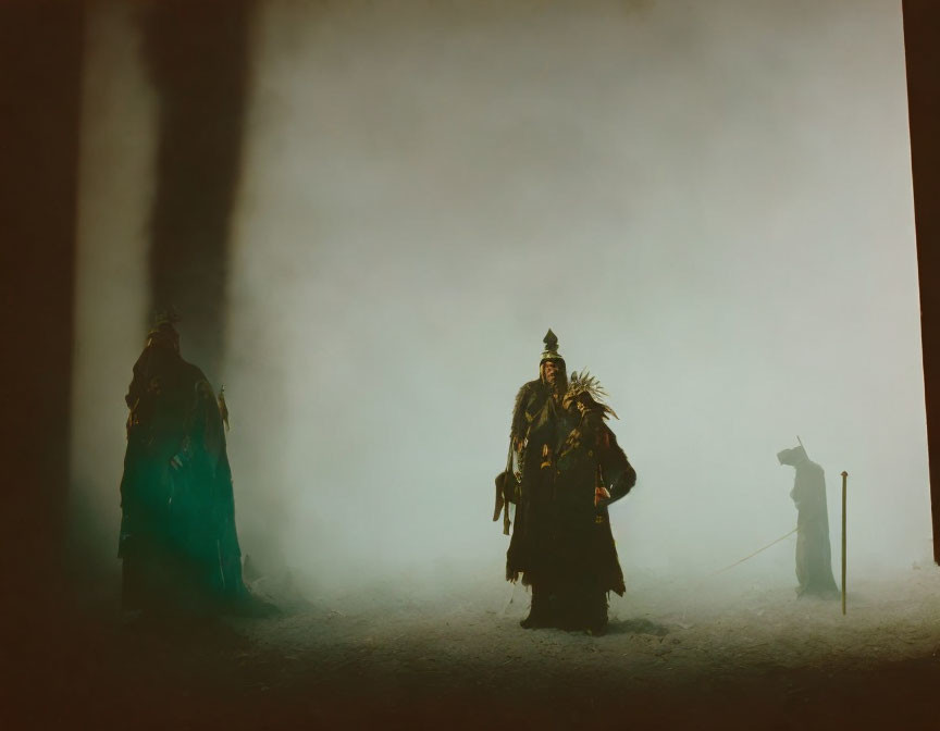 Three mysterious figures in elaborate costumes in somber foggy setting