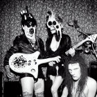 Three individuals in skull makeup with a guitar on a tinsel backdrop.