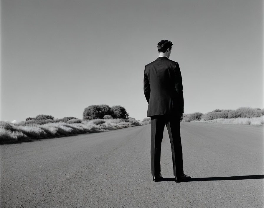 Man in suit on empty road with flat terrain and sparse vegetation under clear sky