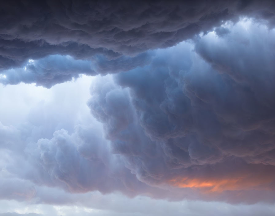 Varied shades of blue and grey dramatic thunderclouds with orange glow on horizon