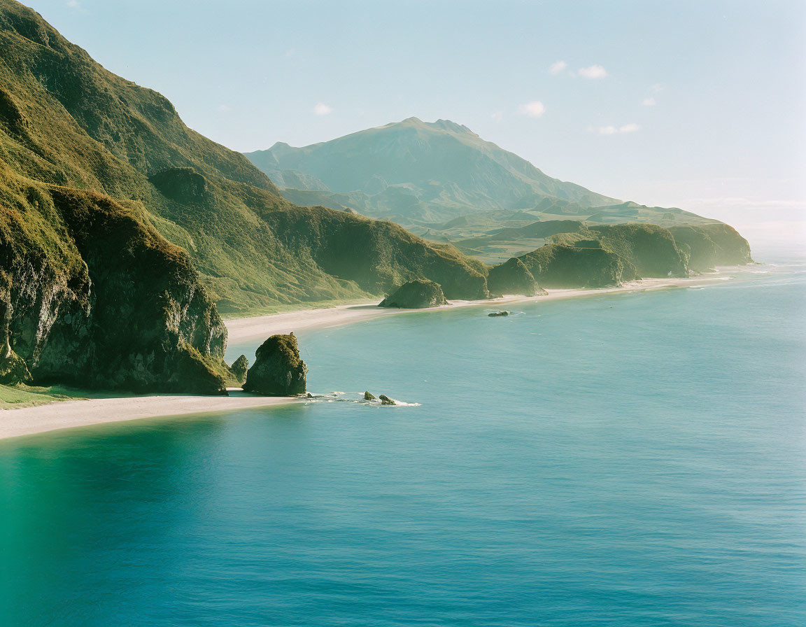 Scenic coastal landscape with green cliffs, blue sea, and distant mountain