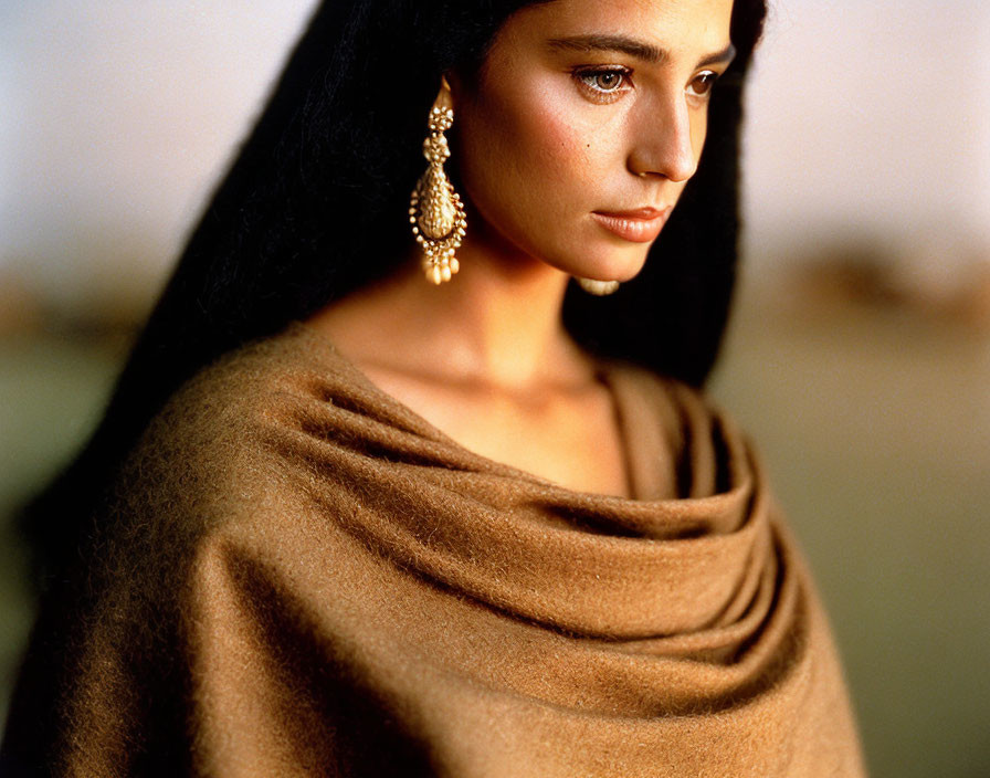 Portrait of woman with dark hair and golden earrings in softly lit setting