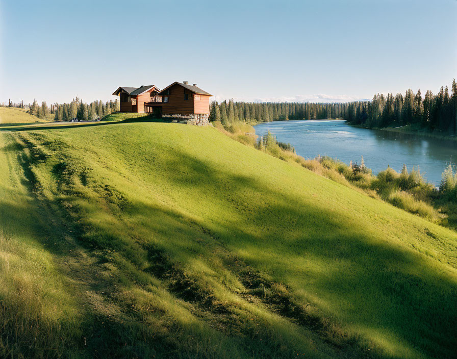 Tranquil landscape: wooden house on green hill by calm river