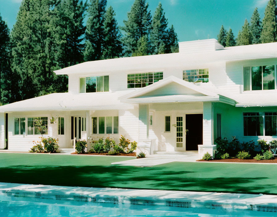 Spacious white modern house with trees, pool, and blue sky