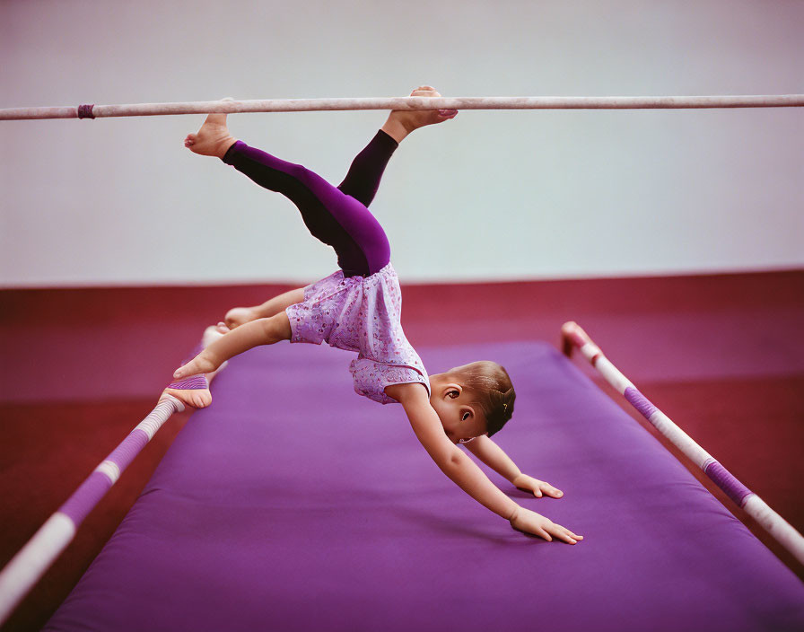 Young gymnast practicing on uneven bars with one hand gripping lower bar