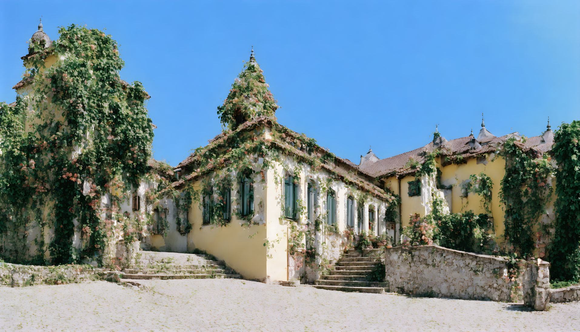 Ivy-covered baroque building with towers and staircase under blue sky