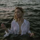 Blond woman in wet white shirt emerges from water