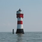 Monochromatic lighthouse on rocky outcrop with dramatic sky & rough sea waves