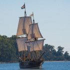 Colorful ornate ship sailing near lush green hills and mountains on calm waters.