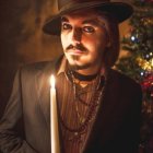 Man in hat holding candle with warm lighting & autumn leaves.