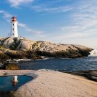 Scenic lighthouse on rocky cliff with crashing waves under sunny sky