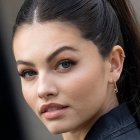 Close-up portrait of woman with striking blue eyes, dark hair, subtle makeup, in dark green outfit