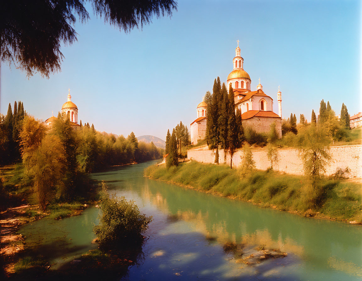 Tranquil river surrounded by greenery, leading to church with golden domes