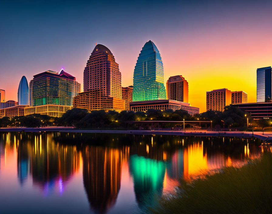 City skyline at sunset with reflections on river and modern buildings.