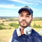 Stylized male figure with cap and ear piercings against rural backdrop