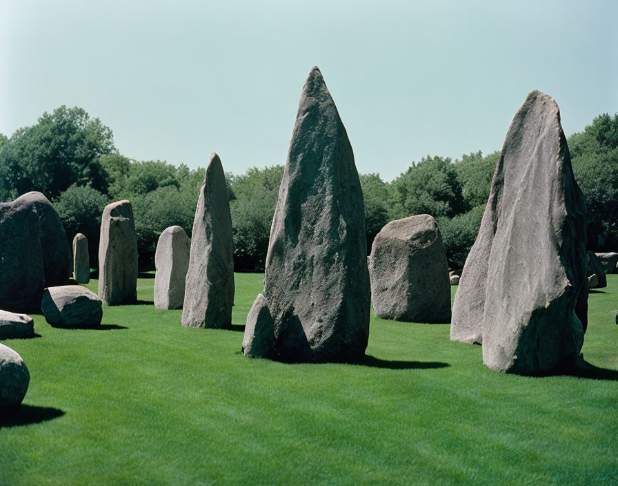 Ancient standing stones in grassy field with trees on sunny day