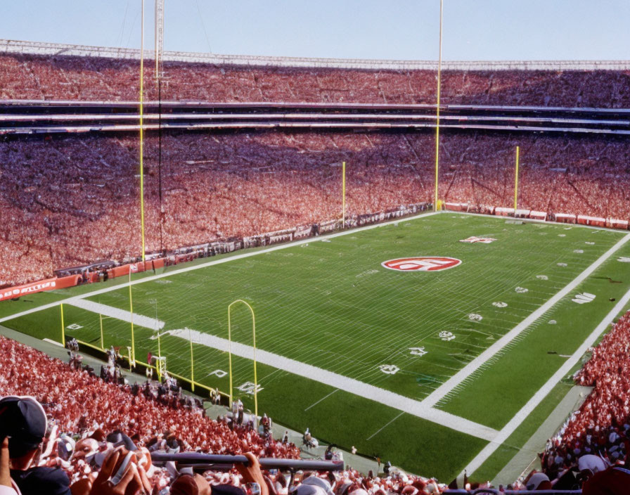 Crowded stadium with red-clad spectators watching football on sunny day.