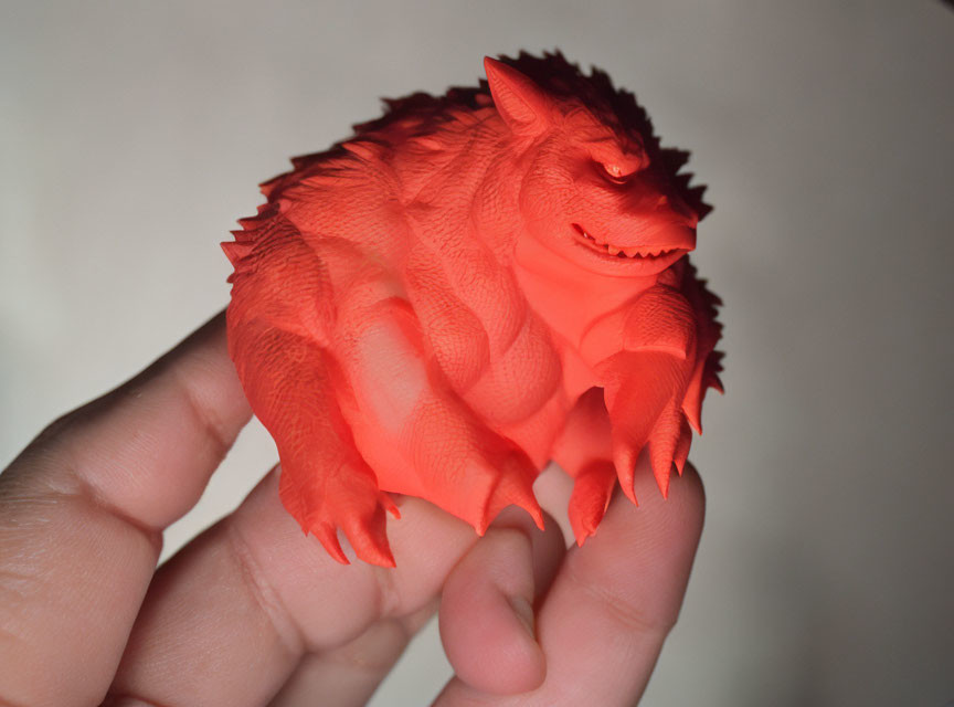 Red spiky monster figurine held by hand