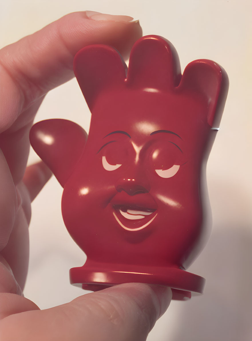 Red Smiling Cartoonish Glove Character Held by Hand on Light Background