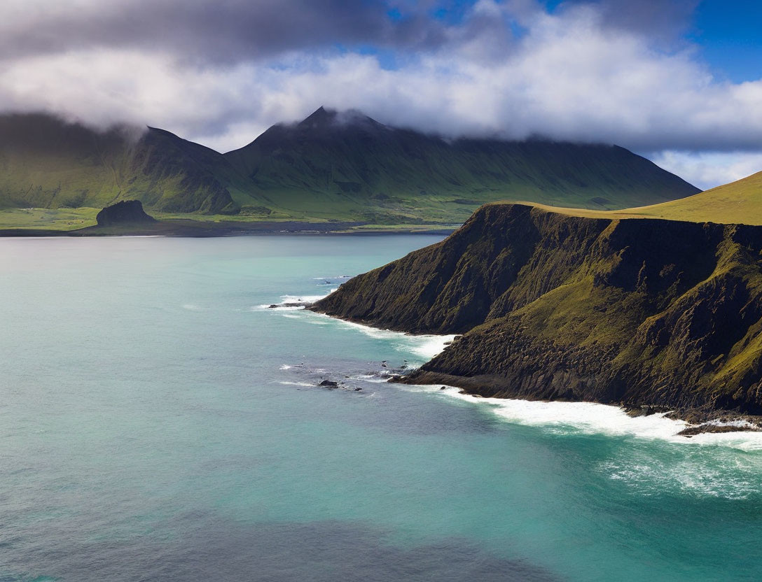 Tranquil coastal scene: green mountains, blue waters, gentle waves, rocky cliffs.