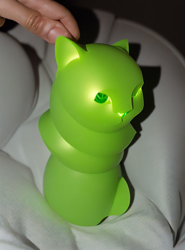 Glowing green cat-shaped lamp with spiral design on white surface