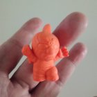 Orange humanoid plastic toy with smiling face held in hand