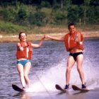 Colorfully dressed women waterskiing together on calm river with forest background