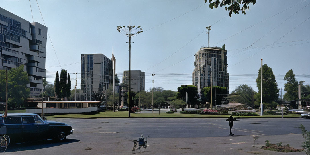 Tranquil street scene with modern buildings, trees, person walking dog, vintage car