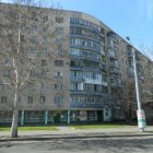 Curved office building with glass facade and balconies, set against clear blue sky and bare trees.