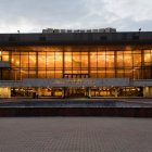 Contemporary building with large glass windows, flat roof, and sunset reflection, set against dusk sky and