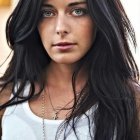 Portrait of woman with long dark hair, blue eyes, freckles, white top, layered neck