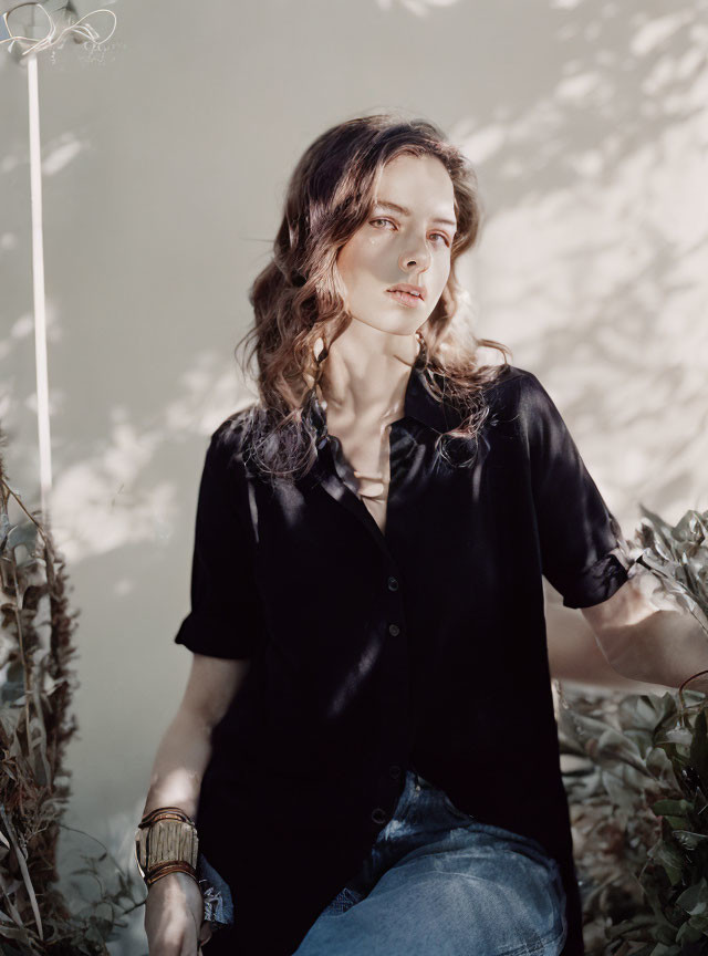 Woman in black shirt and jeans sitting surrounded by greenery and soft light