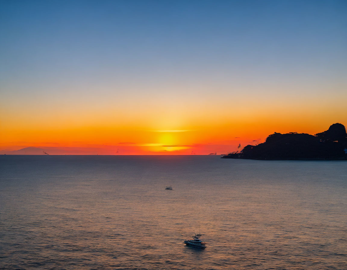 Tranquil sunset seascape with orange and blue skies, silhouetted landforms, and