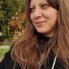 Young girl with wavy brown hair in dark coat and scarf.