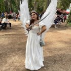 Angel with white wings in blue gown gazes at vibrant forest.