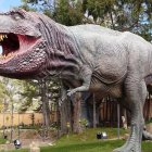 Detailed dinosaur sculpture in park setting with lush trees