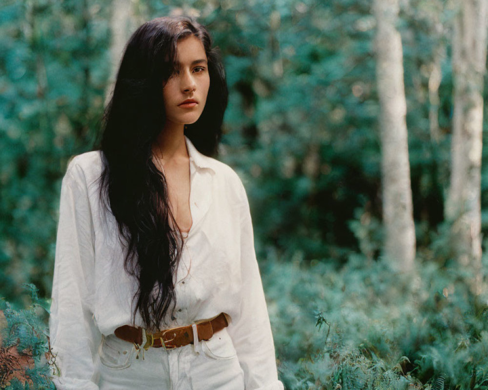 Woman in white shirt and pants standing in lush forest setting