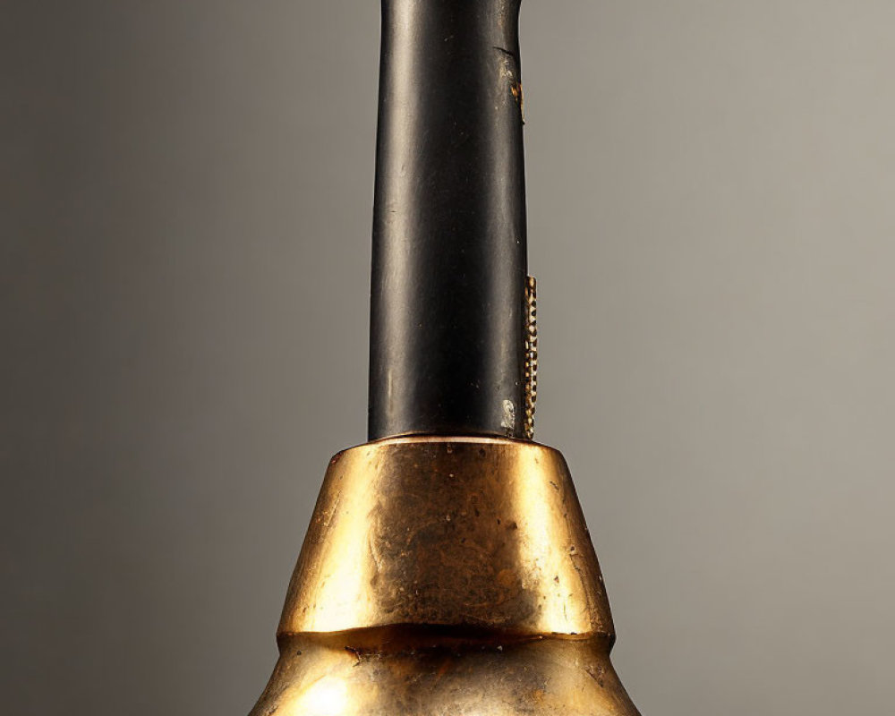 Aged brass and black bell handle with tarnish on neutral background