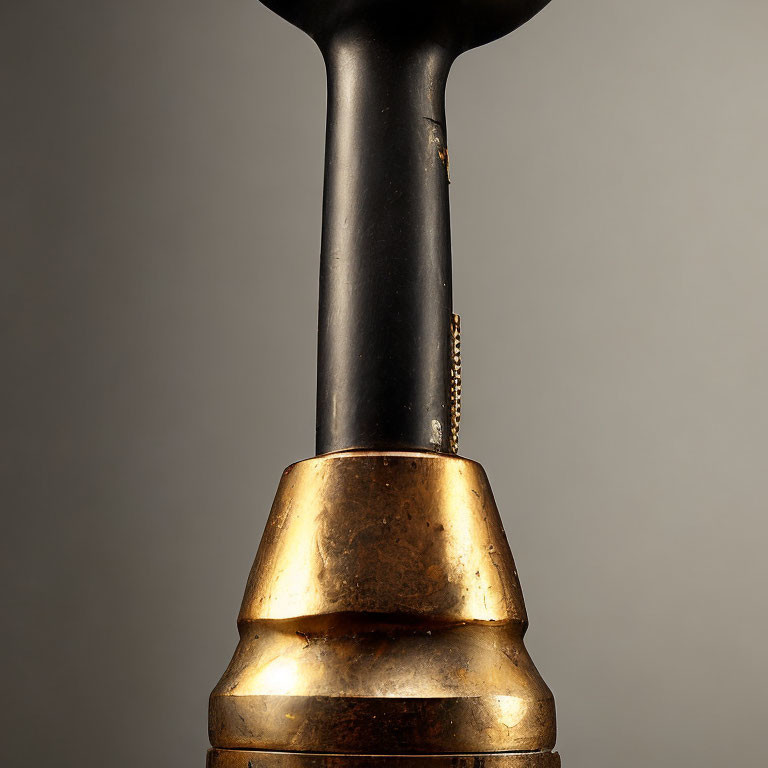 Aged brass and black bell handle with tarnish on neutral background