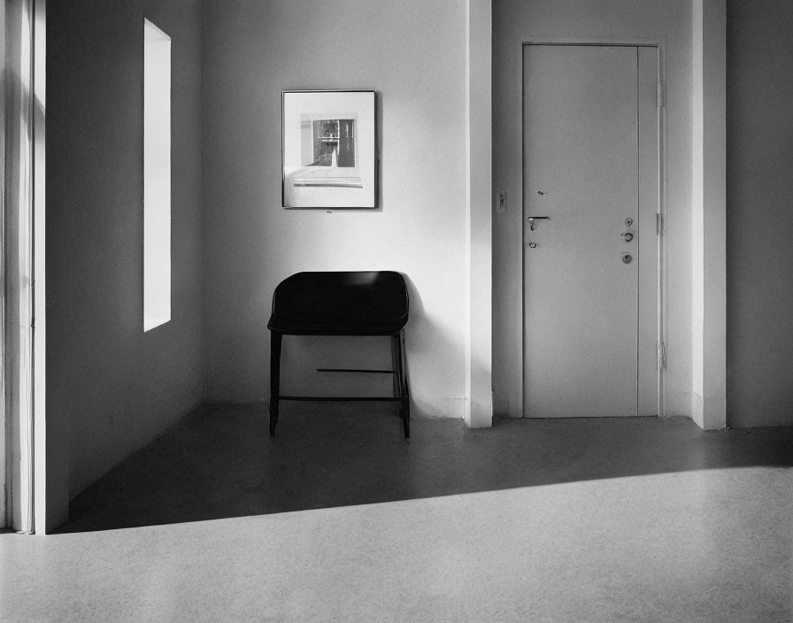 Monochrome image: Empty room with bench, picture, door, sunlight shadows